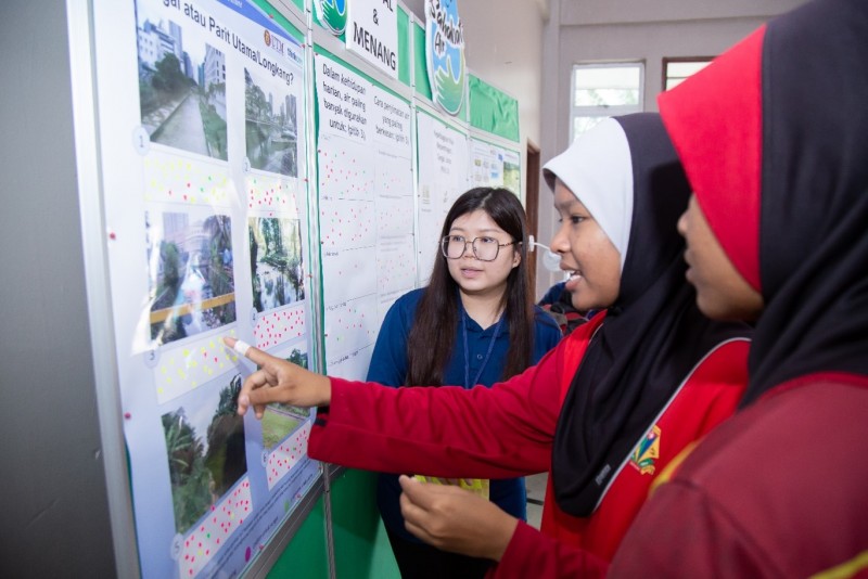 Neo from the Malaysia team chats with two female school pupils are they look at a wall display